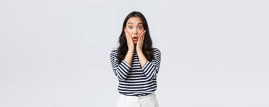 Yaşam tarzı, insanların duyguları ve gelişigüzel kavramlar. Şaşırmış soluk soluğa kadın etkilenmiş bakıyor, duygularını ifade edemiyor, çenesini indiriyor ve yüzüne dokunuyor şaşkınlık içinde, beyaz arka planda duruyor.