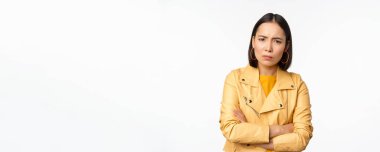 Asyalı bir kızın kızgın ve incinmiş görünümü, üzgün, gücenmiş yüz ifadesi, beyaz arka planda dikilmesi.