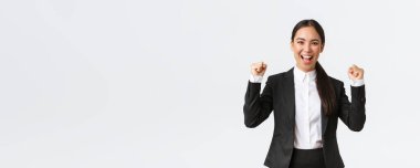 Başarılı siyah takım elbiseli kadın girişimci, yumruk tokuşturma ve bağırma evet heyecanlı, zaferi kutluyor. İş kadını beyaz arka planda büyük başarı elde ediyor.