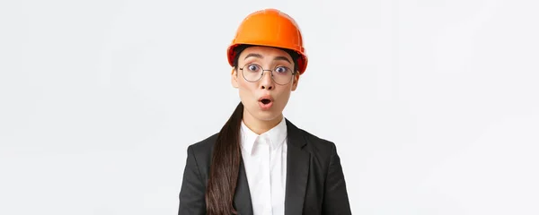 Primer plano de sorprendido y preocupado asiático ingeniero escuchar malas noticias, anuncio preocupante, de pie en máscara de seguridad, gafas y traje de negocios y jadeo sobresaltado, fondo blanco —  Fotos de Stock