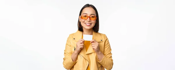 Портрет улыбающейся корейской модели в солнцезащитных очках, с кредитной картой, стоящей на белом фоне — стоковое фото