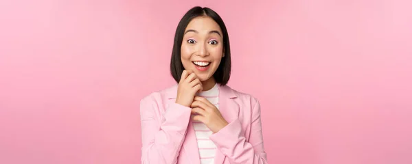 Glad ung kontorsdam, koreansk affärskvinna klädd i kostym, ser förvånad ut över kameran, poserar mot studio bakgrund i rosa — Stockfoto
