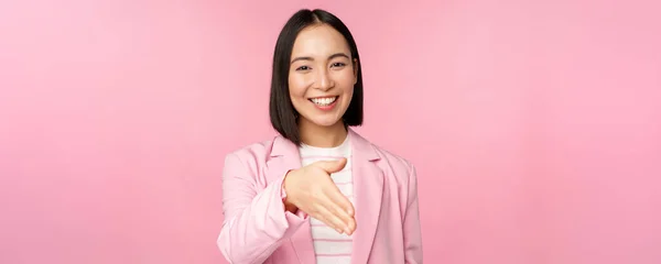 미소짓는 기분좋은 사업가가 사업 파트너와 악수를 하고 손을 뻗고 분홍색 배경 위에 서서 인사를 하는 모습 — 스톡 사진