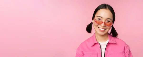 Close up de menina coreana elegante em óculos de sol, sorrindo feliz, posando contra fundo rosa. As pessoas enfrentam conceito — Fotografia de Stock