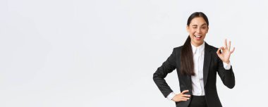 İddialı ve kendinden emin Asyalı genç iş kadını kontrol altına alındı, göz kırp ve anlaşmayı teşvik etmek için iyi bir hareket göster, iyi iş, iyi iş ya da onay jesti, mutlu ayakta durmak