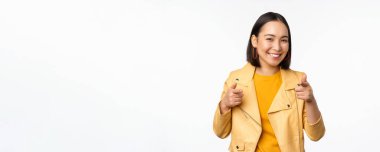 Hey sen! Mutlu gülümseyen Asyalı kadın kamerayı işaret ediyor, seni seçiyor, tebrik ediyor ve övüyor, beyaz arka plana karşı duruyor.