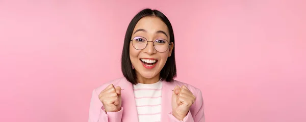 Nahaufnahme Porträt einer asiatischen Geschäftsfrau, die jubelt, nach der sie Ausschau hält, voller Hoffnung und Begeisterung in die Kamera blickt, lächelt und lacht, vor rosa Hintergrund steht — Stockfoto