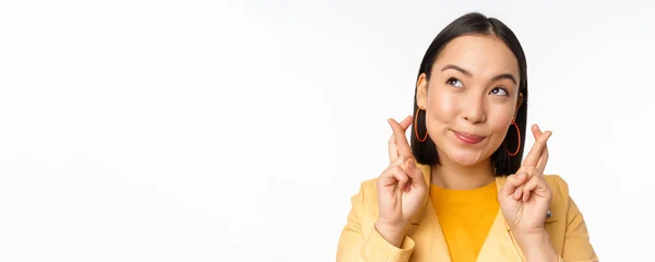 Primer plano retrato de la chica asiática esperanzada que desea, dedos cruzados para la buena suerte, orando y sonriendo, de pie sobre fondo blanco — Foto de Stock