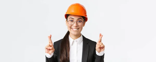 興奮したアジアの女性エンジニアのクローズアップ,安全ヘルメットとおいしいのために嘆願ビジネススーツの建設マネージャー,クロス指幸運とかむ唇魅力的な,白の背景 — ストック写真