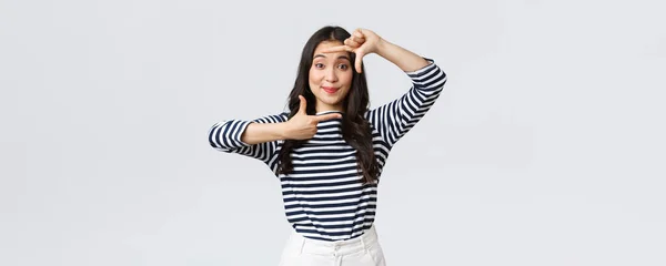 Mode de vie, émotions des gens et concept décontracté. créatif mignon asiatique fille picturing capture moment avec main cadres geste sourire amusé rester positif et heureux fond blanc — Photo