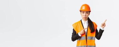 İnşaat, inşaat ve endüstriyel konsept. Üzgün ve hayal kırıklığına uğramış Asyalı yönetici, güvenlik miğferi takan mühendis, kötü bir şeyden yakınıyor, parmaklarını sağ üst köşeyi işaret ediyor.