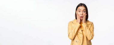 Şaşırmış, şaşırmış, şok olmuş, beyaz arka planda duran Asyalı bir kadın görüntüsü.