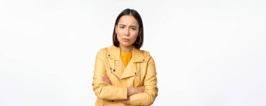 Asyalı bir kızın kızgın ve incinmiş görünümü, üzgün, gücenmiş yüz ifadesi, beyaz arka planda dikilmesi.