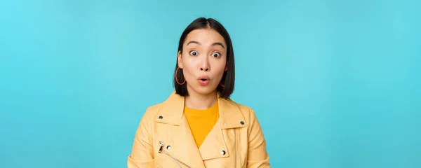 Close up portrait of asian girl looks surprised at amazed, wow face expression, stands over blue background — Stock Photo, Image