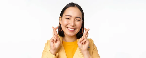 Close up portrait of hopeful asian girl wishing, cross fingers for good luck, praying and smiling, standing over white background — Stock Photo, Image