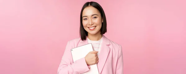 Image d'une jeune femme d'entreprise coréenne, PDG tenant une tablette numérique, souriant et regardant professionnel, portant un costume, debout sur fond rose — Photo