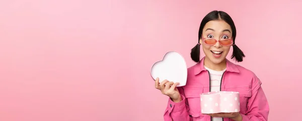 Carino ragazza asiatica che ti dà regalo in scatola a forma di cuore, baci e sorrisi, concetto di vacanza e celebrazione, in piedi su sfondo rosa — Foto Stock