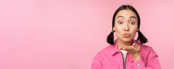 Close up ritratto di bella sciocca ragazza asiatica, l'invio di aria bacio, mwah a macchina fotografica, soffiando, in piedi su sfondo rosa — Foto Stock