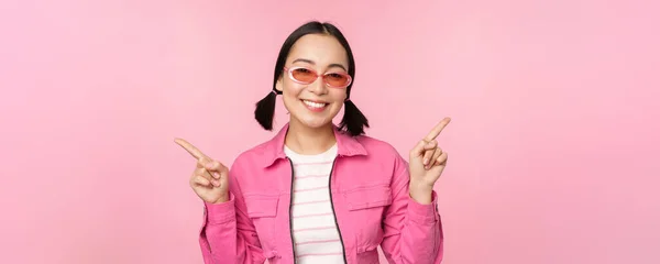 Elección. Elegante chica coreana, modelo femenino asiático señala los dedos de lado, muestra dos variantes, anuncio de producto, elementos de demostración, de pie sobre fondo rosa —  Fotos de Stock
