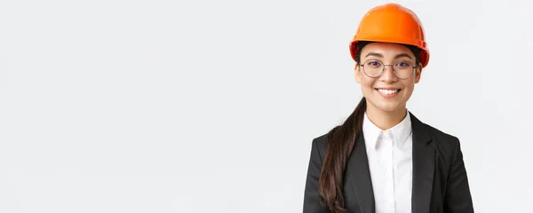 Крупним планом усміхнений професійний азіатський інженер-жінка, бізнес-леді в костюмі і безпечному шоломі, що має огляд на заводі, виглядає впевнено і задоволений, стоячи білий фон — стокове фото