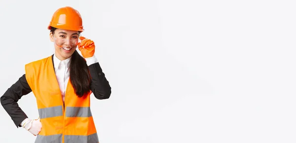 Zelfverzekerde succesvolle Aziatische vrouwelijke chief manager op zoek trots en glimlachend naar camera, het dragen van veiligheidshelm, bril en handschoenen in de bouw of onderneming, witte achtergrond — Stockfoto