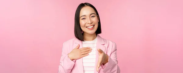 Retrato de sorridente, agradável empresária apertando as mãos com parceiro de negócios, aperto de mão, estendendo a mão e dizendo olá, de pé sobre fundo rosa — Fotografia de Stock