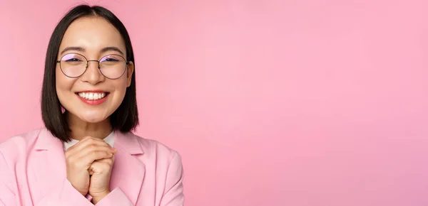 Close up portrait of smiling happy businesswoman in glasses, clench hands together thankful, excited of smth, begging or say please, standing over pink background