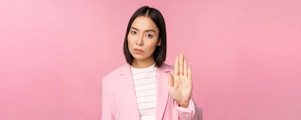 亚洲女商人，表情严肃，关心面子，表现出停止动作，忌讳，禁止手势，不赞成恶臭，站在粉红的背景上 — 图库照片