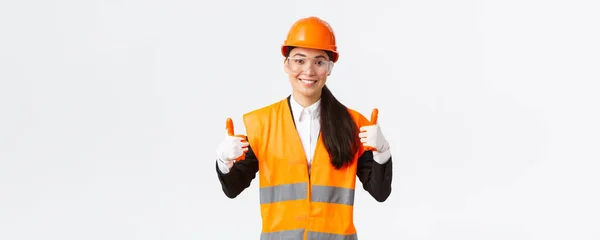 Satisfecho sonriente mujer asiática jefe de ingeniería de construcción dando permiso para entrar en el edificio o entertprise después de usar ropa de seguridad, gafas guantes y casco, mostrando los pulgares hacia arriba en la aprobación —  Fotos de Stock