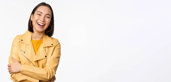 Immagine di bella ragazza asiatica moderna che ride, sorride e guarda felice alla macchina fotografica, in piedi in giacca gialla sullo sfondo bianco — Foto Stock