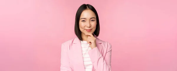 Imagem de mulher de negócios asiática em pé em pose de pensamento, brainstoming, vestindo terno. Vendedora coreana, empresária posando contra fundo rosa — Fotografia de Stock