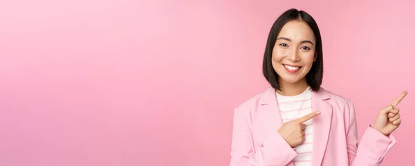 Entusiasta donna d'affari professionale, commessa punta il dito destro, mostrando pubblicità o logo aziendale da parte, posa su sfondo rosa — Foto Stock