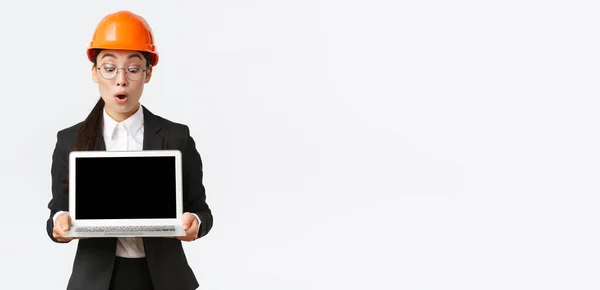 Beeindruckte asiatische Bauingenieurin, Architektin oder Managerin im Unternehmen zeigt Laptop-Bildschirm mit verblüfftem Gesichtsausdruck, schaut bei Besprechungen auf Gewinndiagramm, trägt Schutzhelm in Fabrik — Stockfoto