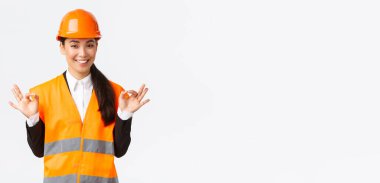 Mimar mükemmel bir plan yaptı. Güvenlik kaskı takmış kendine güvenen Asyalı kadın mühendis her şeyi kontrol altında tutuyor, mükemmel sonuçlardan memnun, beyaz arka planda duruyor.