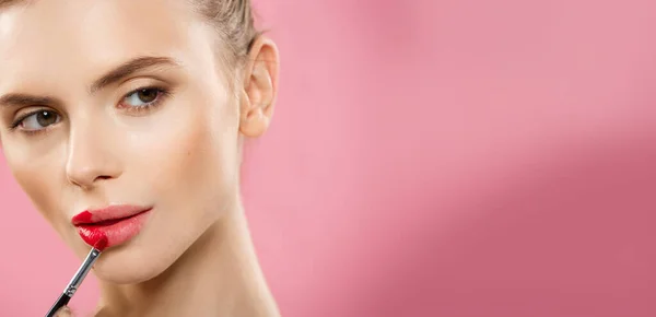 Beauty Concept - Woman applying red lipstick with pink studio background. Beautiful girl makes makeup. — Stock Photo, Image