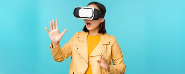 Fiatal ázsiai nő használ virtuális valóság szemüveg, VR headset, álló vicces ellen kék háttér — Stock Fotó