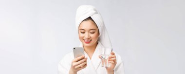 Su içen sağlıklı genç, güzel bir kadın, doğal makyajla yüz yüze, cep telefonuyla, beyaz arka planda izole edilmiş..