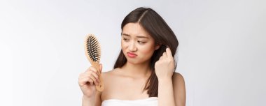 Üzüntülü genç Asyalı kadın, beyaz izole arka planda ellerinde saçı olan kuru saçlı..