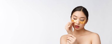 Asyalı güzel bir genç kadın, gözlerinin altında altın maskelerle cildini önemser..