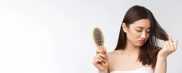 Rozrušený stresu mladá asijská žena drží poškozené suché vlasy na rukou přes bílé izolované pozadí. — Stock fotografie