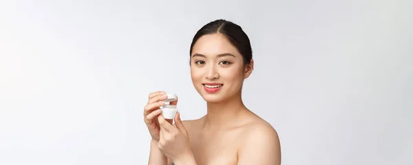 Красива молода жінка на білому ізольованому фоні, тримає косметичний крем для обличчя, азіатський — стокове фото