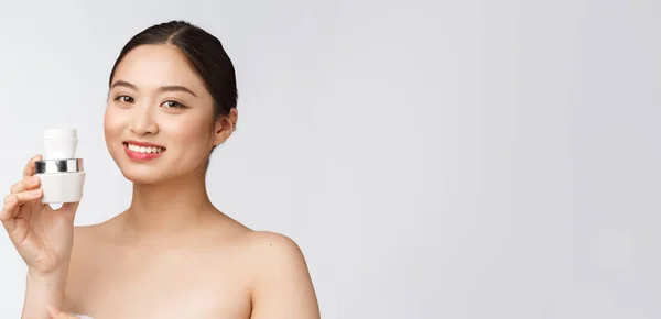 Gyönyörű fiatal nő fehér elszigetelt háttér gazdaság kozmetikai arc krém, ázsiai — Stock Fotó