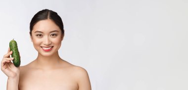 Asyalı genç bir kadın soyutlanmış arka planda salatalık tutuyor..