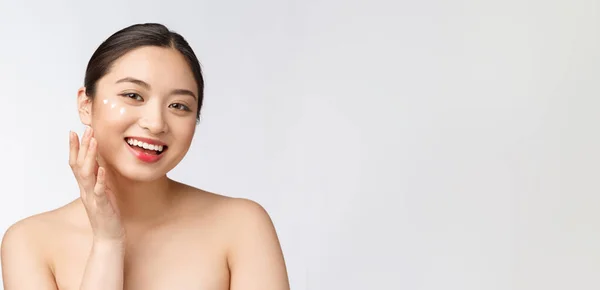 피부는 미녀를 돌봅니다. 미녀가 크림바르면서 웃고 있어. 흰색에 고립된 아름다운 아시아인 여성 모델의 아름다운 초상화. — 스톡 사진