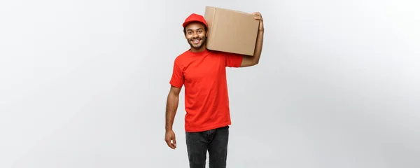 Concepto de entrega - Retrato del hombre de entrega afroamericano feliz en tela roja sosteniendo un paquete de caja. Aislado en Grey studio Background. Copiar espacio . —  Fotos de Stock