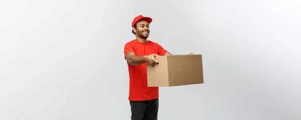 Conceito de entrega - Retrato de homem de entrega afro-americano feliz em pano vermelho segurando um pacote de caixa. Isolado no estúdio Grey Background. Espaço de cópia . — Fotografia de Stock