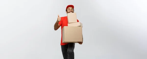 Conceito de entrega - Retrato de homem de entrega afro-americano feliz segurando embalagens de caixa e mostrando thumps para cima. Isolado no estúdio Grey Background. Espaço de cópia . — Fotografia de Stock