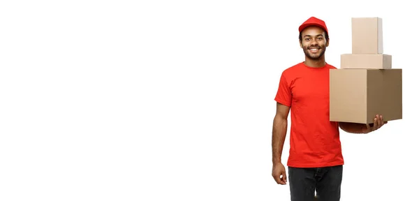 Concepto de entrega - Retrato del hombre de entrega afroamericano feliz en tela roja sosteniendo un paquete de caja. Aislado en fondo de estudio blanco. Copiar espacio — Foto de Stock