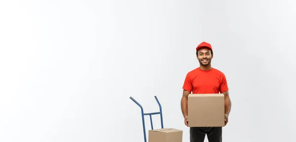 Lieferkonzept - Porträt eines gut aussehenden afrikanisch-amerikanischen Zustellers oder Kuriers mit Handwagen und Transportbox. isoliert auf grauem Studiohintergrund. Kopierraum. — Stockfoto