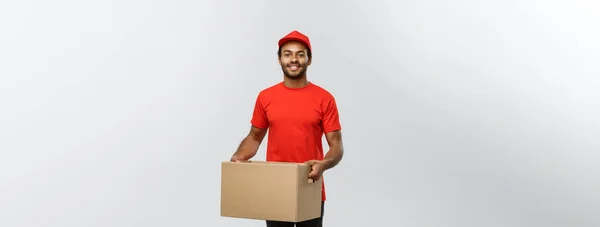 Koncepcja dostawy - Portret szczęśliwego Afroamerykanina w czerwonej tkaninie trzymającego paczkę. Odizolowany na szarym tle studia. Przestrzeń kopiowania. — Zdjęcie stockowe
